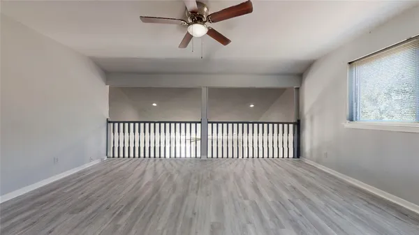 an empty room with wooden floor a ceiling fan and windows
