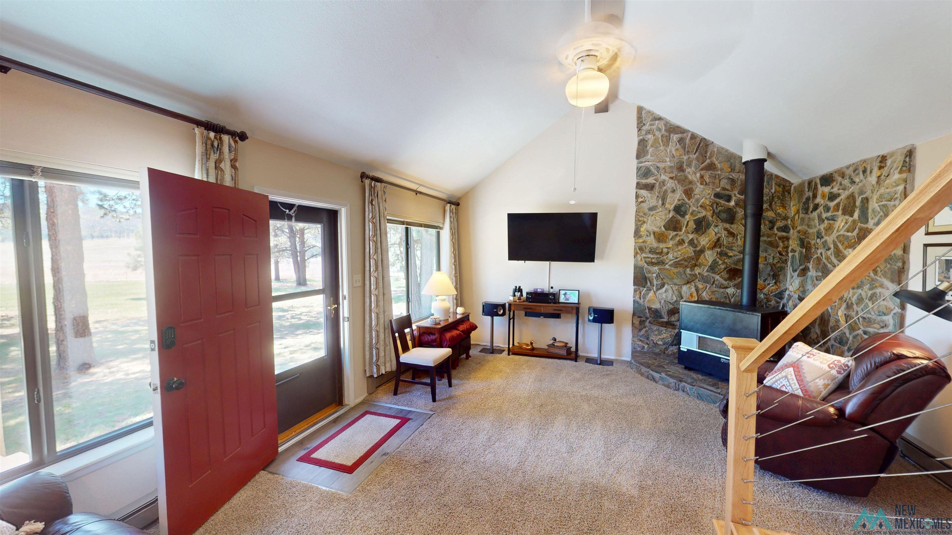 23 Pendaries Lane Rociada, NM 87742 - Photo 3 of 26 Vaulted ceiling living space featuring a wood-burning stove with a stone surround, large windows, and neutral carpeting