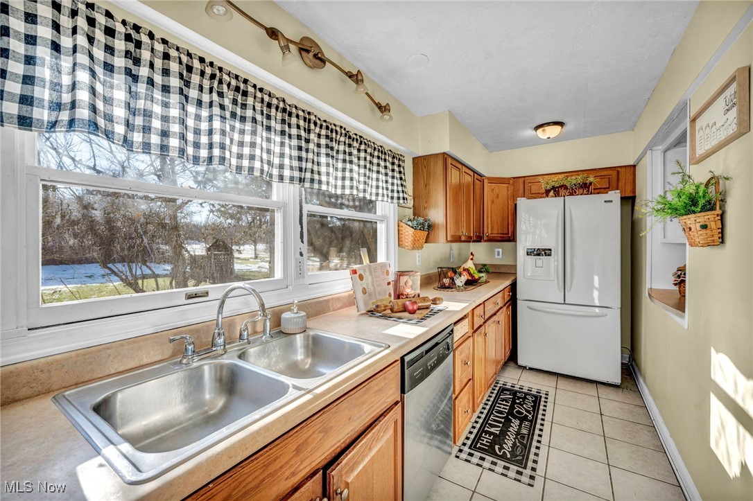 5948 South Ridge Road West Geneva, OH 44041 - Photo 5 of 16 Kitchen with white fridge with ice dispenser, light tile patterned floors, light countertops, dishwasher, and brown cabinets