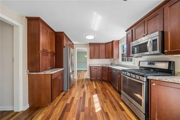 a kitchen with stainless steel appliances granite countertop a stove a sink dishwasher a microwave oven and a refrigerator with wooden floor