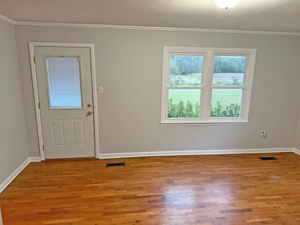 a view of an empty room with wooden floor and a window