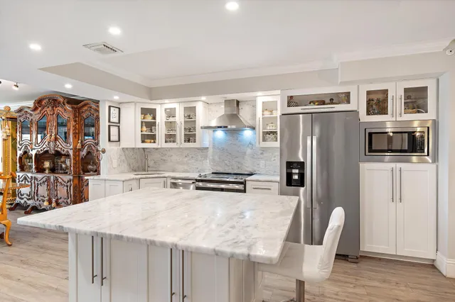 a kitchen with stainless steel appliances granite countertop a refrigerator a stove a sink a dining table and chairs with wooden floor