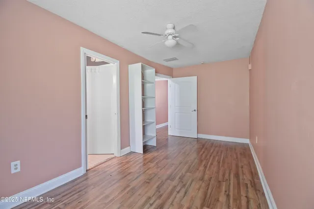 an empty room with wooden floor chandelier fan and windows
