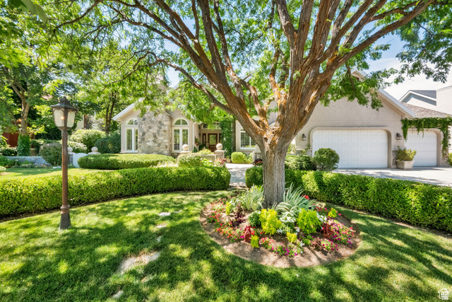 7740 Keswick Road Sandy, UT 84093 - Photo 2 of 74 Stone and stucco exterior featuring arched windows, an attached two-car garage, mature shade trees, manicured hedges, and established garden beds