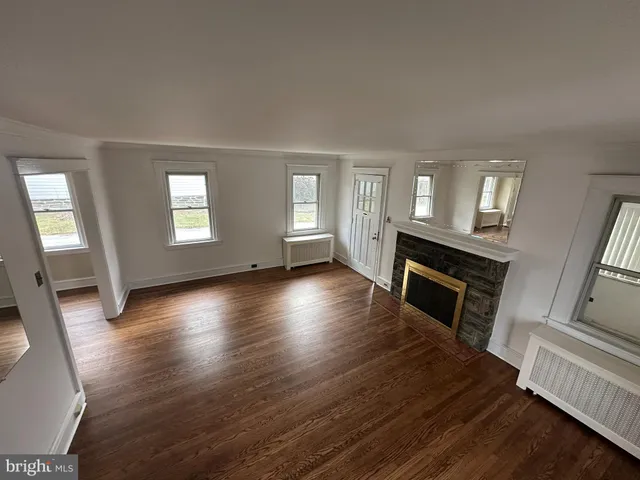 an empty room with wooden floor fireplace and windows