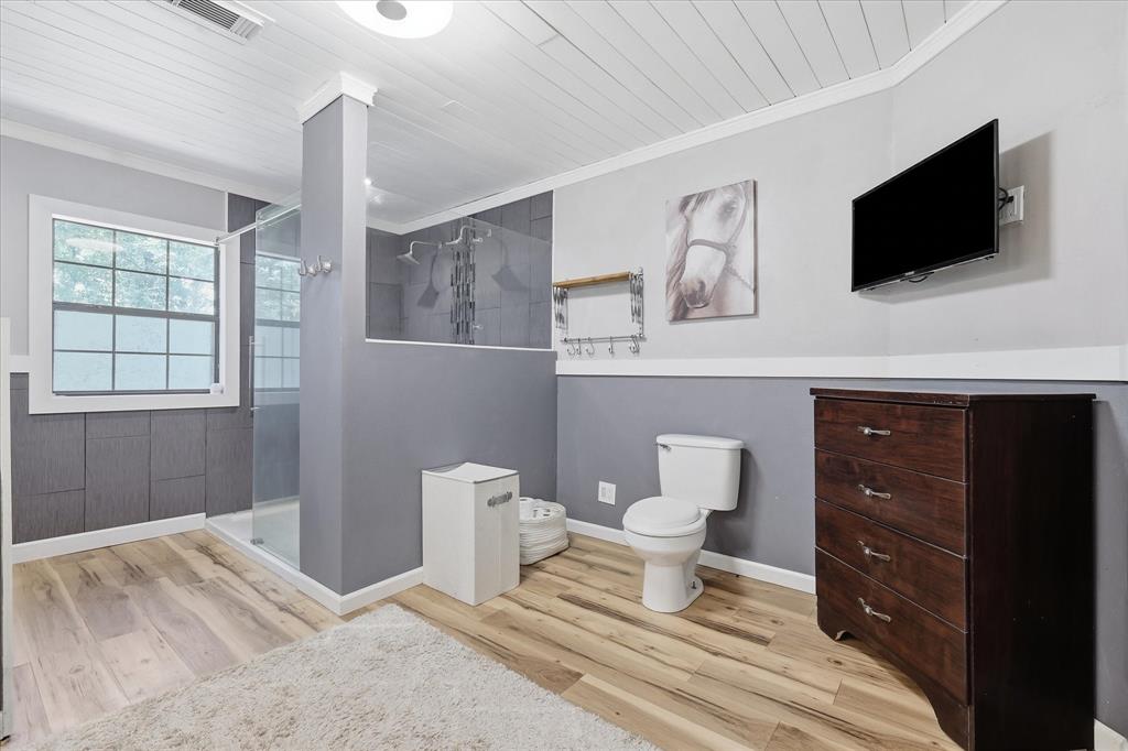 237 Brenda Lane Gainesville, TX 76240 - Photo 20 of 40 Bathroom featuring wood-finish flooring, a glass-enclosed shower with multiple showerheads, a window, and paneled walls