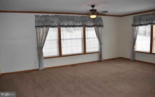 an empty room with chandelier fan and windows