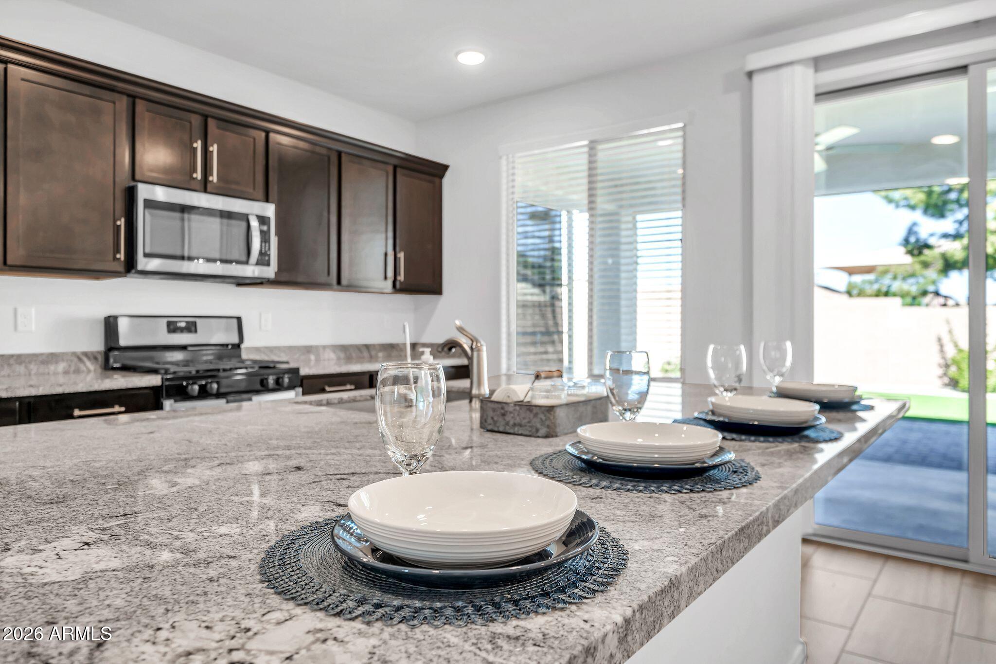 14384 West Hearn Road Surprise, AZ 85379 - Photo 8 of 63 a kitchen with stainless steel appliances kitchen island granite countertop a stove a sink a refrigerator dining table and chairs