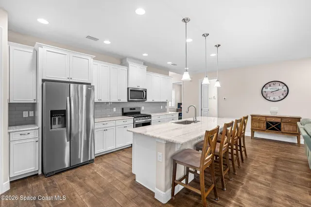 a kitchen with stainless steel appliances kitchen island granite countertop a dining table chairs refrigerator and stove