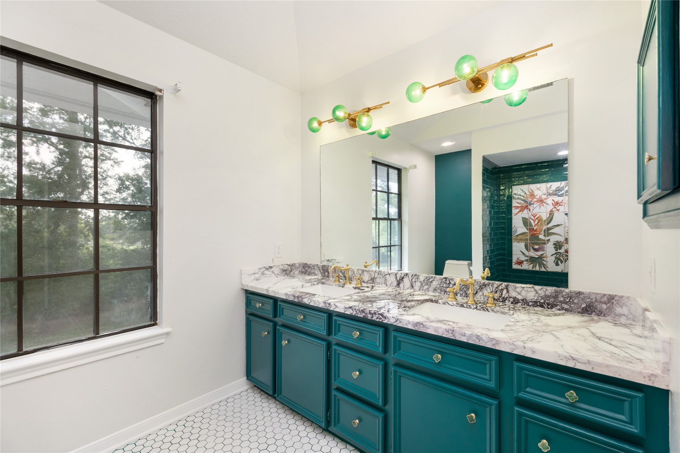 17003 Creeksouth Road Houston, TX 77068 - Photo 33 of 49 Bold cabinetry adds a vibrant touch beneath dual sinks with sleek marble counters, while large windows and eye-catching modern light fixtures enhance the room’s fresh, artistic vibe. A perfect blend of function and flair.