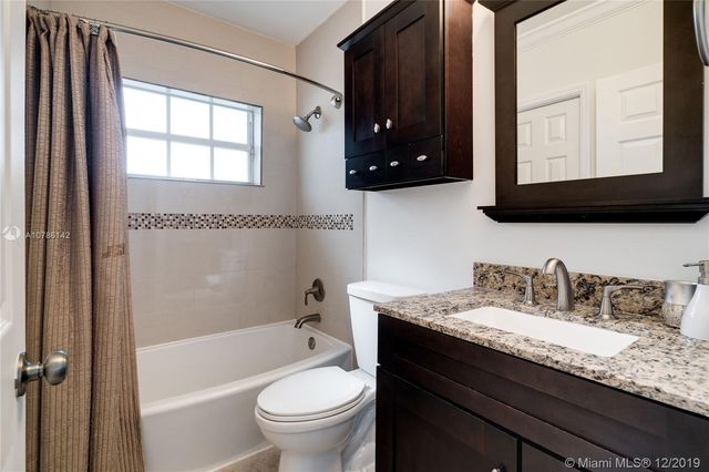 a bathroom with a granite countertop sink toilet mirror and bathtub