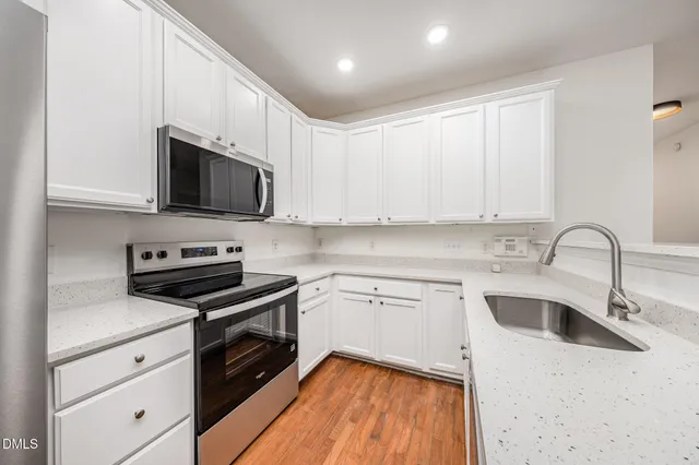 a kitchen with stainless steel appliances granite countertop a sink a stove top oven a refrigerator with white cabinets and stainless steel appliances