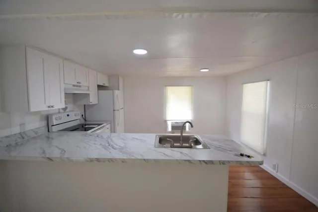 a view of a kitchen with a sink stove wooden cabinets and entryway