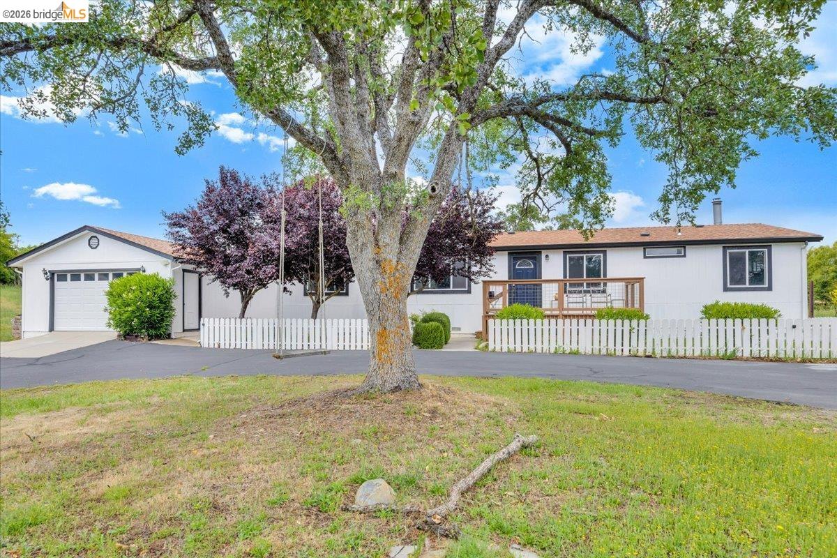 4419 Little John Road Copperopolis, CA 95228 - Photo 2 of 43 White exterior featuring a front deck with wood railings, a white picket fence, and a paved driveway leading to an attached garage