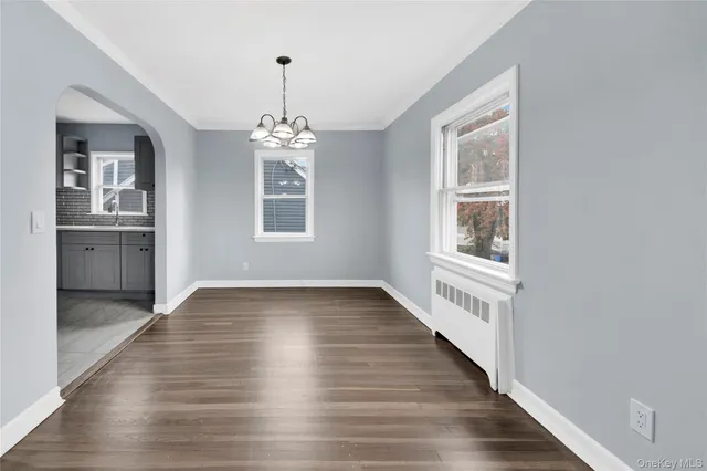 an empty room with wooden floor chandelier and windows