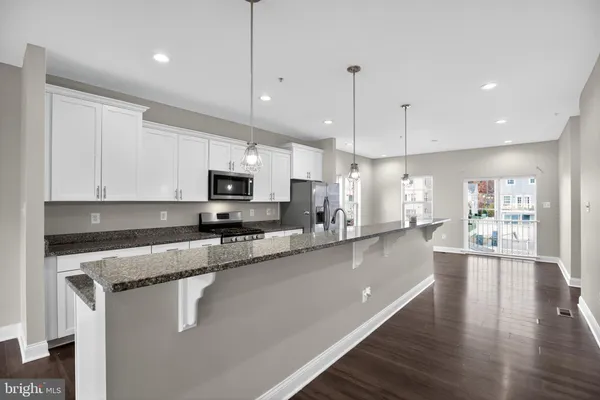 a large kitchen with stainless steel appliances granite countertop a stove a sink a microwave oven a large island with white cabinets and wooden floor