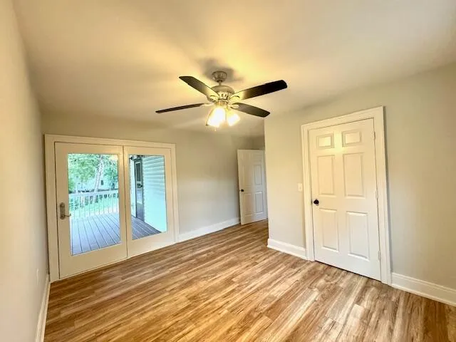 a view of an empty room with wooden floor and a ceiling fan