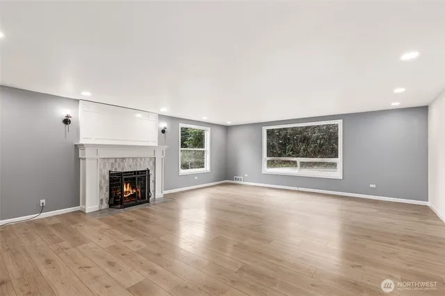 a view of an empty room with wooden floor fireplace and a window