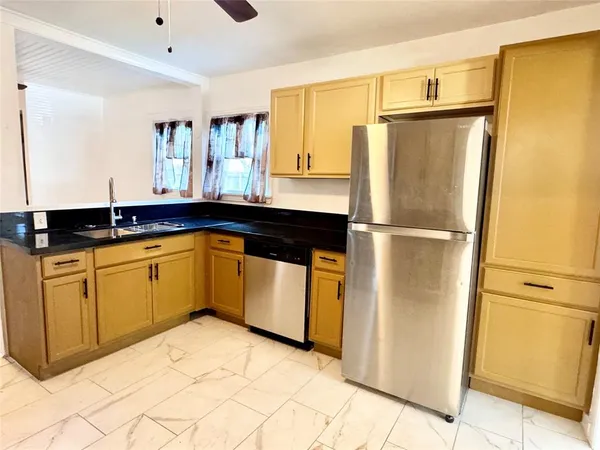 a kitchen with granite countertop a refrigerator a sink and white cabinets