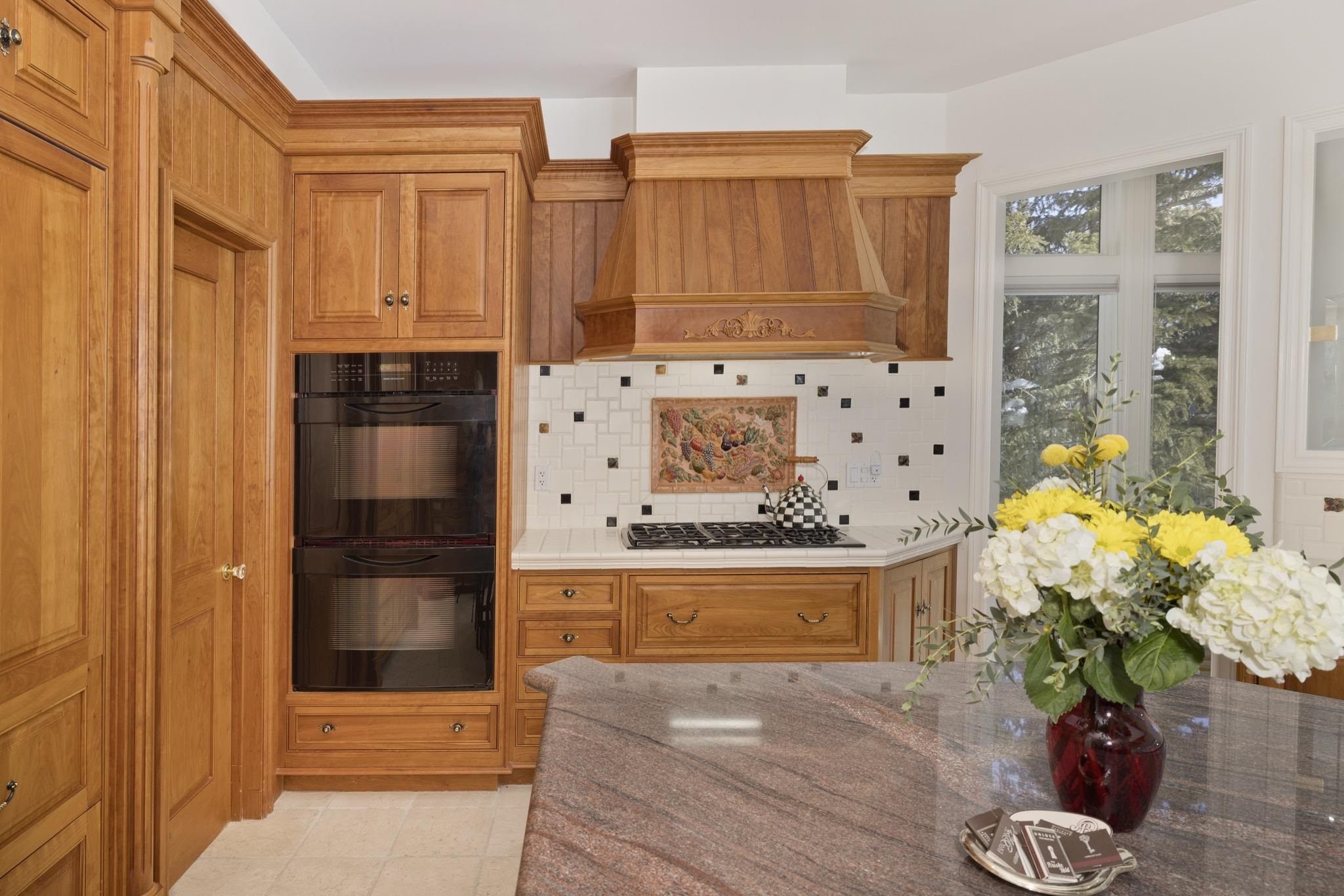 370 Ranch Road Mammoth Lakes, CA 93546 - Photo 10 of 46 Kitchen featuring brown cabinetry, backsplash, light stone counters, premium range hood, and light tile patterned floors
