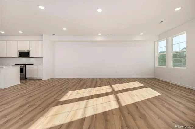 a view of empty room with wooden floor and kitchen view