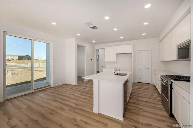 a kitchen with stainless steel appliances granite countertop a stove a refrigerator a sink and white cabinets with wooden floor