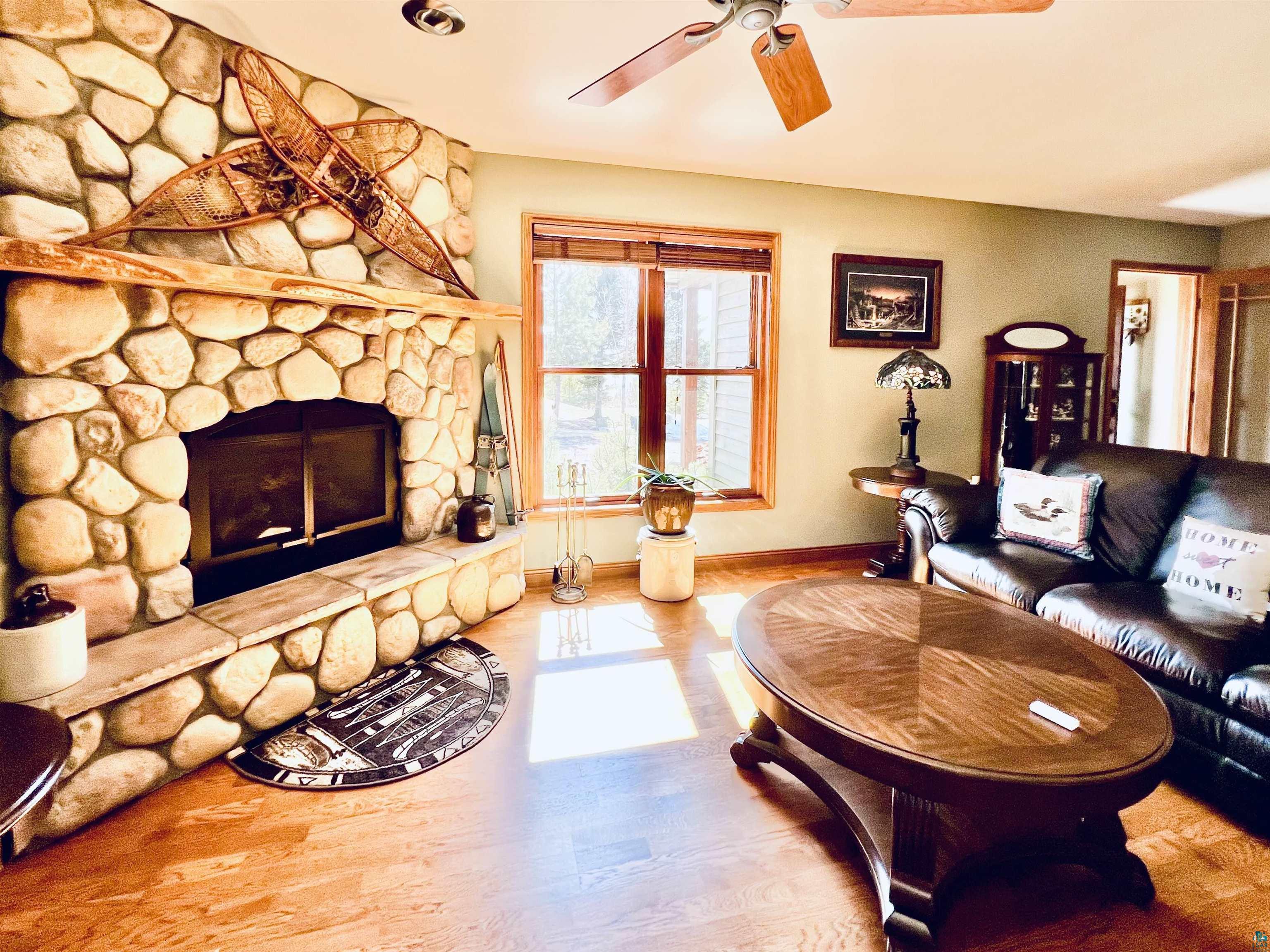 21 Turnagain Trail Lutsen, MN 55612 - Photo 20 of 77 Stone fireplace with a wood mantel and hearth, large window with wood-finish blinds, light wood-finish flooring, and a ceiling fan