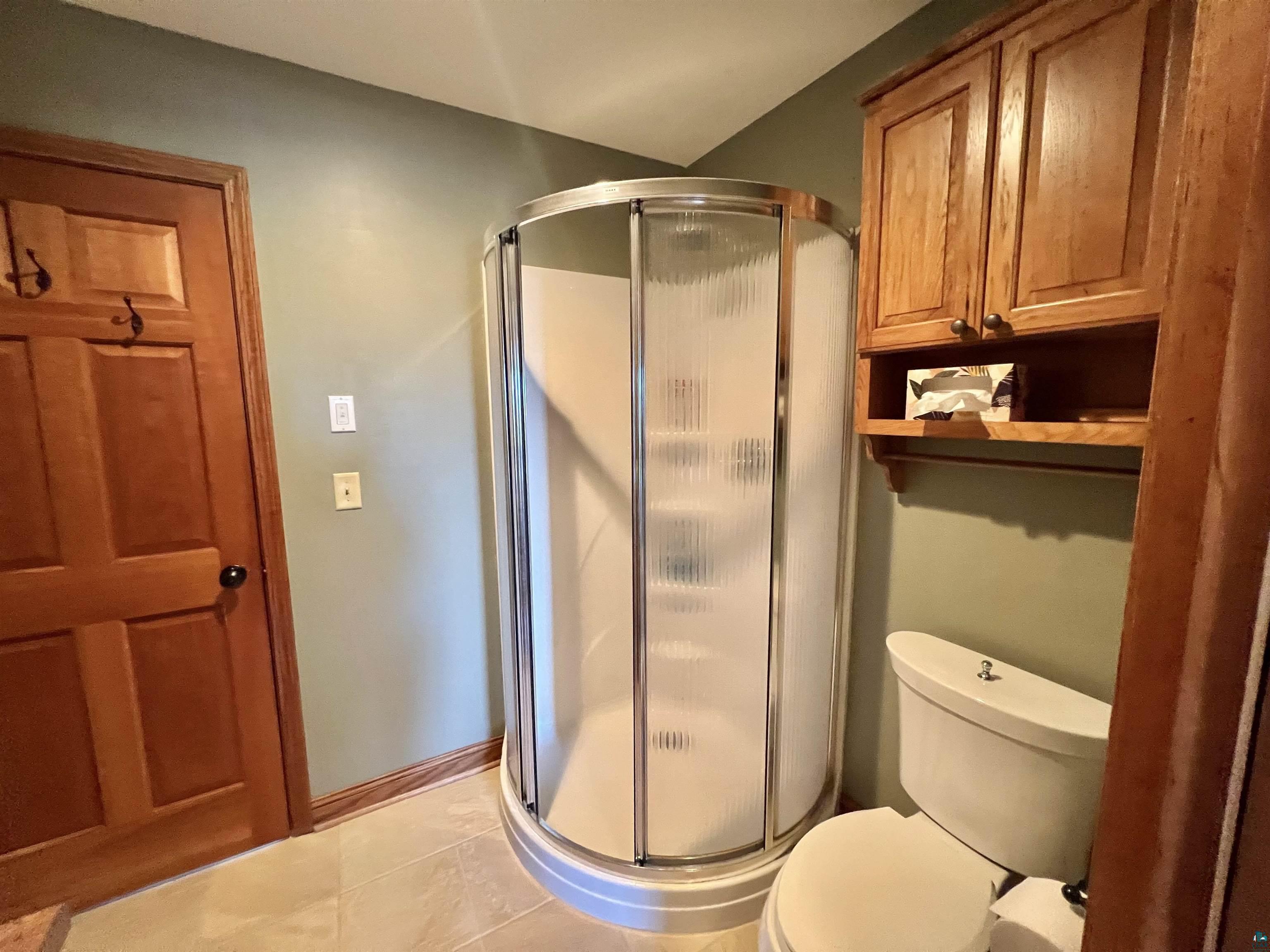 21 Turnagain Trail Lutsen, MN 55612 - Photo 28 of 77 Corner shower enclosure with curved glass doors, a white toilet, and wood cabinetry