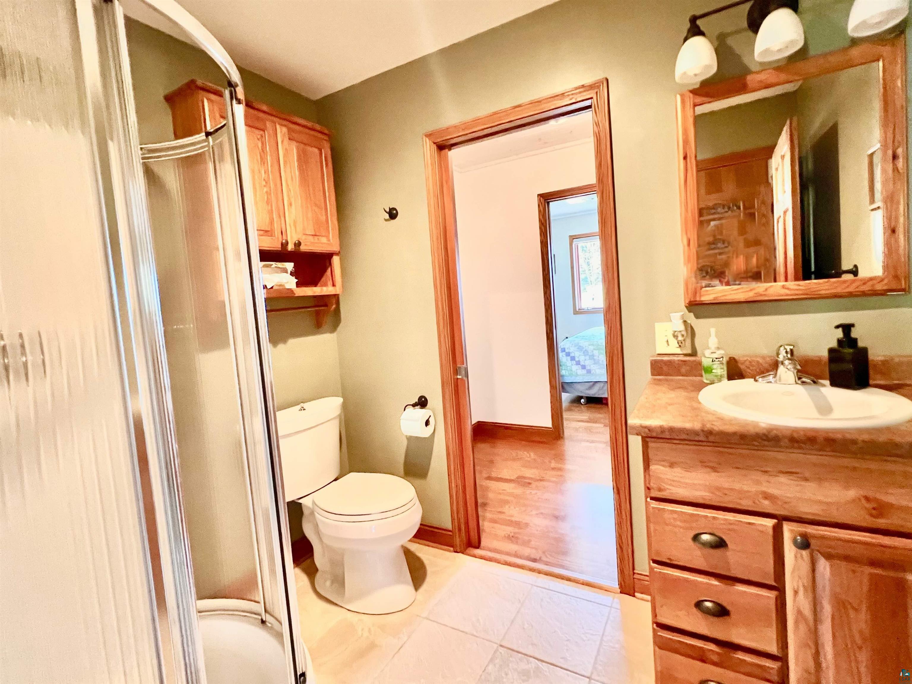 21 Turnagain Trail Lutsen, MN 55612 - Photo 29 of 77 Bathroom featuring a curved glass shower enclosure, wood-finish vanity with an integrated sink, framed mirror, and overhead lighting fixture
