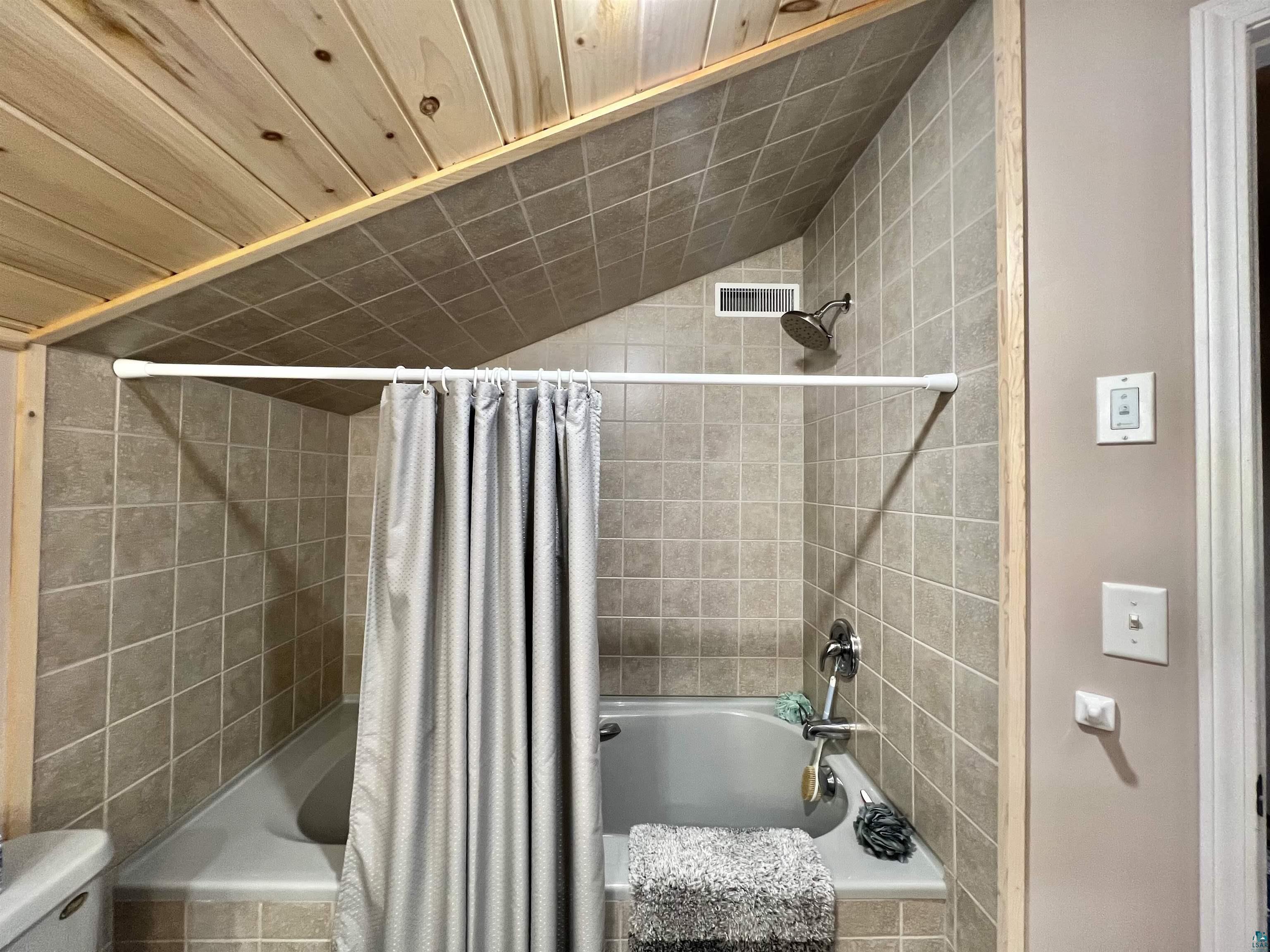 21 Turnagain Trail Lutsen, MN 55612 - Photo 37 of 77 Tiled shower-over-tub with a sloped ceiling featuring wood-plank panels