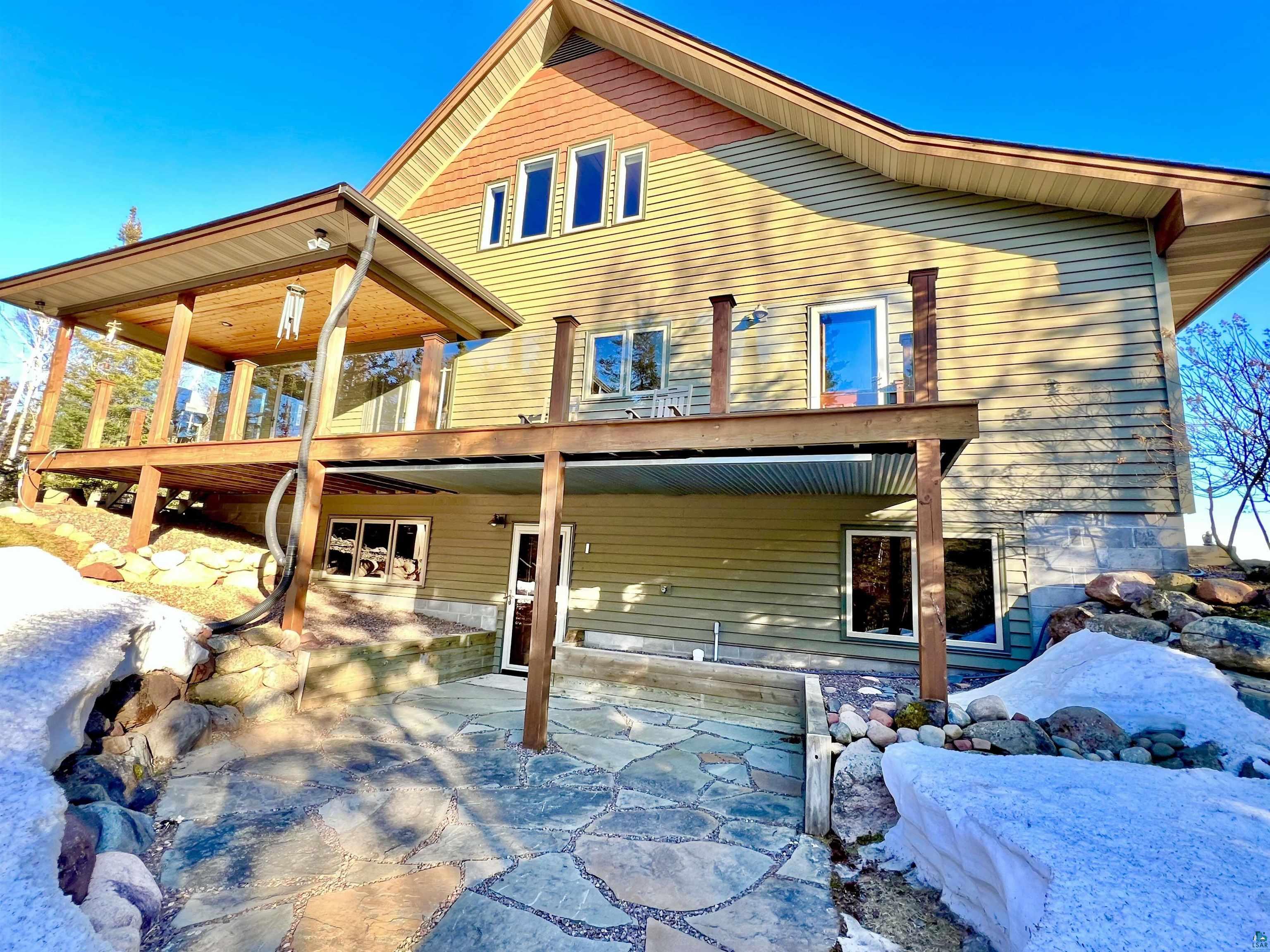 21 Turnagain Trail Lutsen, MN 55612 - Photo 52 of 77 Multi-level residence featuring a covered deck with glass railings, a lower flagstone patio, and a foundational stone facade