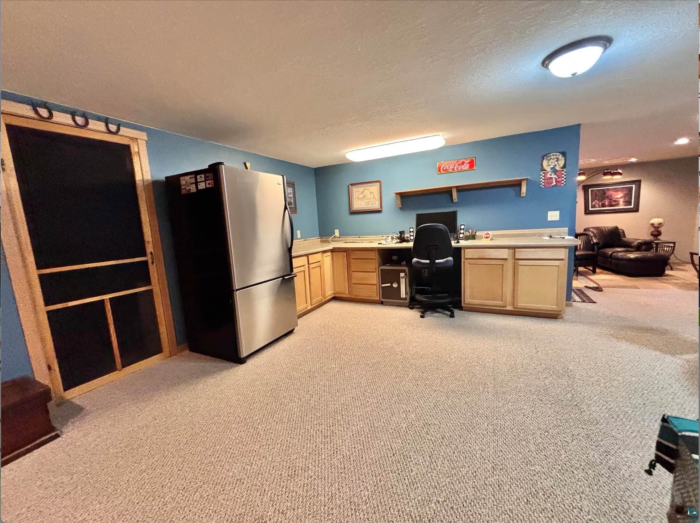 21 Turnagain Trail Lutsen, MN 55612 - Photo 69 of 77 Expansive carpeted area featuring a corner desk with light wood cabinetry, a stainless steel refrigerator, and a partial wall separating spaces