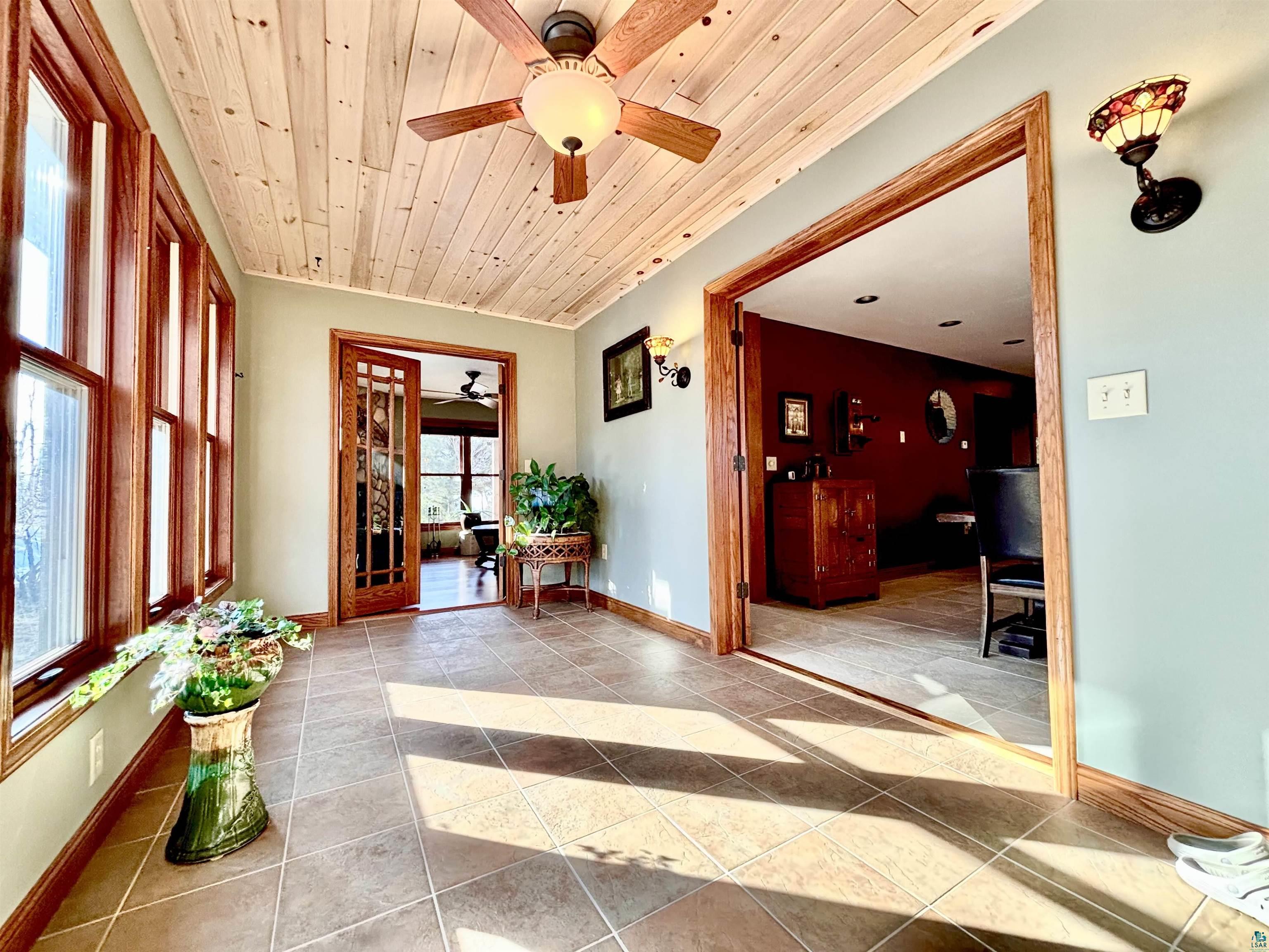 21 Turnagain Trail Lutsen, MN 55612 - Photo 8 of 77 Sun-drenched interior featuring plank wood ceiling, wide window frames, tile flooring, a ceiling fan with integrated lighting, and a glass-paneled door