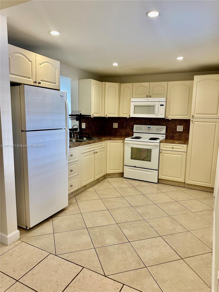 300 Northeast 12th Avenue, Unit 101 Hallandale Beach, FL 33009 - Photo 6 of 23 a kitchen with a refrigerator a stove top oven and a sink with wooden floor