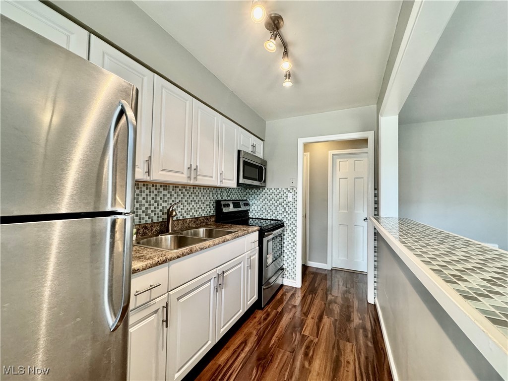 13805 Cedar Road, Unit 103C Cleveland, OH 44118 - Photo 9 of 18 Kitchen featuring dark wood-style flooring, tasteful backsplash, stainless steel appliances, sink, and white cabinetry