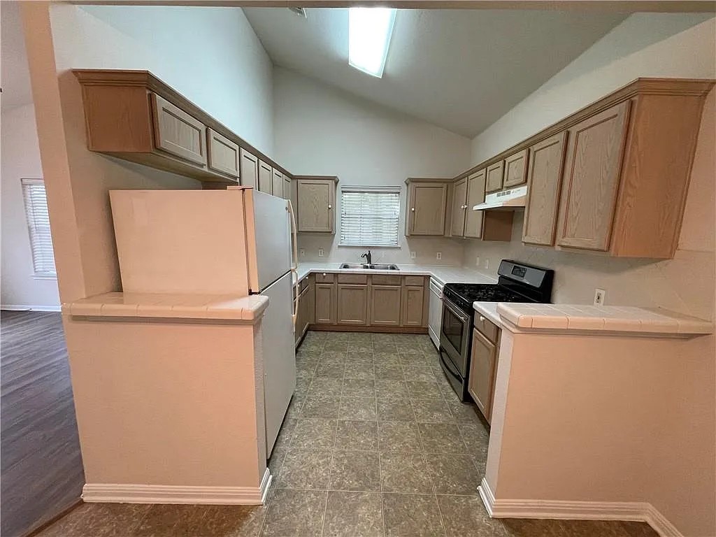 5701 Signal Point Austin, TX 78724 - Photo 4 of 12 Kitchen featuring vaulted ceilings, ample cabinetry, L-shaped countertop, gas range, and a window with blinds