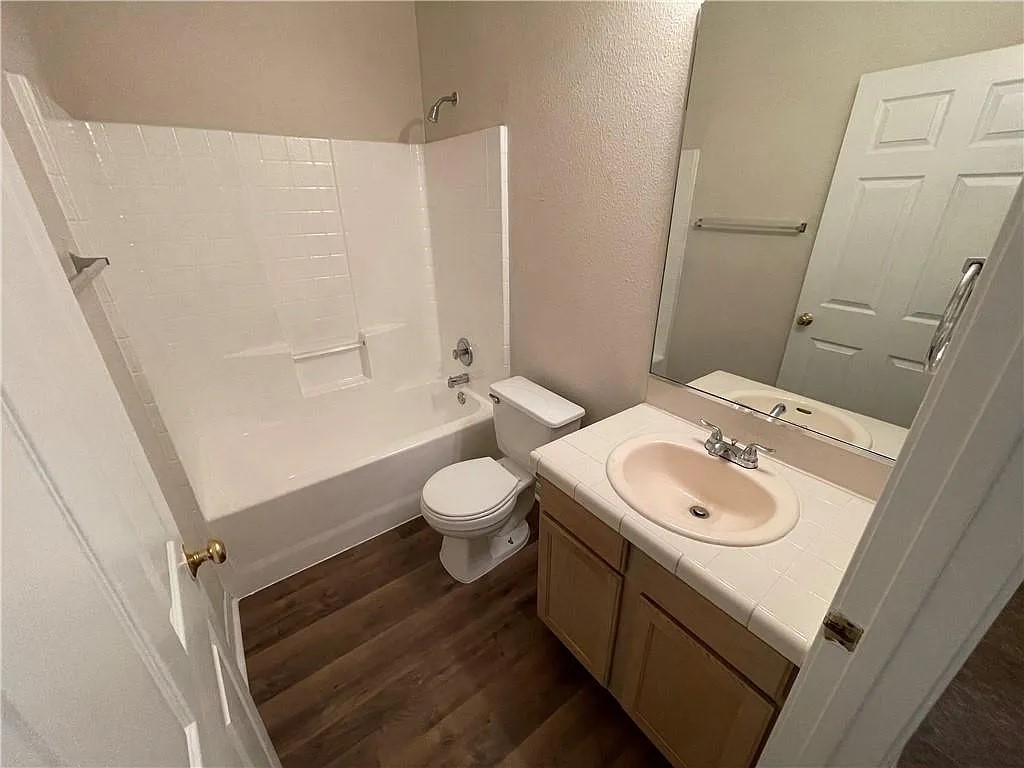 5701 Signal Point Austin, TX 78724 - Photo 10 of 12 Full bathroom featuring a single vanity with tiled countertop, wood-finish flooring, a toilet, and a combined tub and shower with white surround