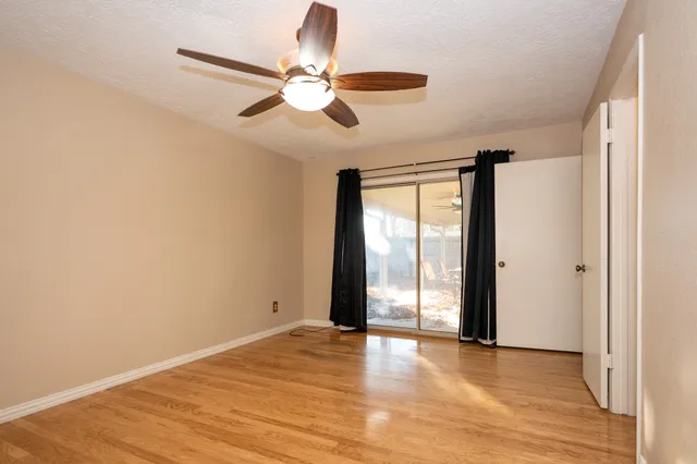 an empty room with wooden floor fan and windows
