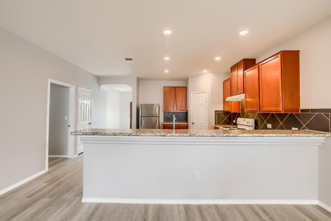 7308 Altidore Drive Austin, TX 78744 - Photo 6 of 24 Kitchen with brown cabinets, a peninsula, freestanding refrigerator, light stone counters, and white stove