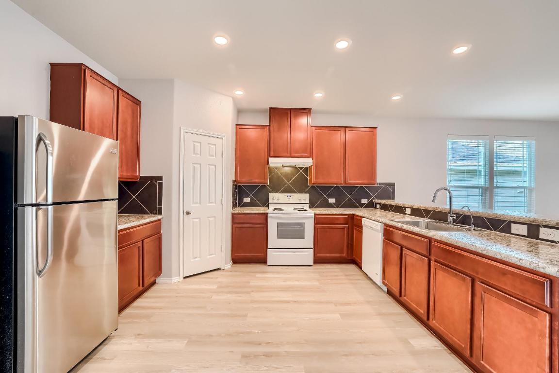 7308 Altidore Drive Austin, TX 78744 - Photo 7 of 24 Kitchen with white appliances, brown cabinetry, light wood-style floors, light stone counters, and recessed lighting