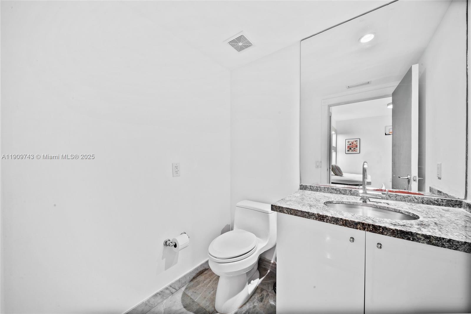 9401 Collins Avenue, Unit 205 Surfside, FL 33154 - Photo 24 of 36 a bathroom with a granite countertop sink a toilet and a mirror