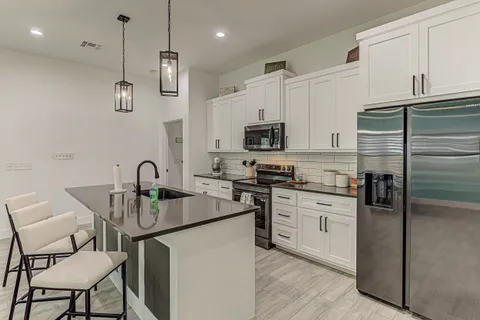 a kitchen with stainless steel appliances a sink a stove a refrigerator cabinets and chairs