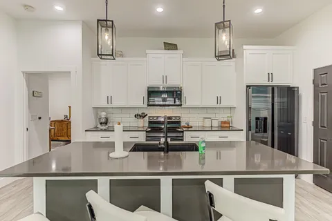 a kitchen with stainless steel appliances granite countertop a sink a stove a refrigerator cabinets and chairs