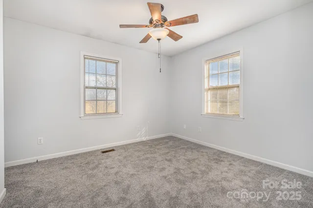 an empty room with chandelier fan and windows