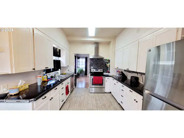 a room with stainless steel appliances kitchen island granite countertop a stove a sink dishwasher and white cabinets with wooden floor