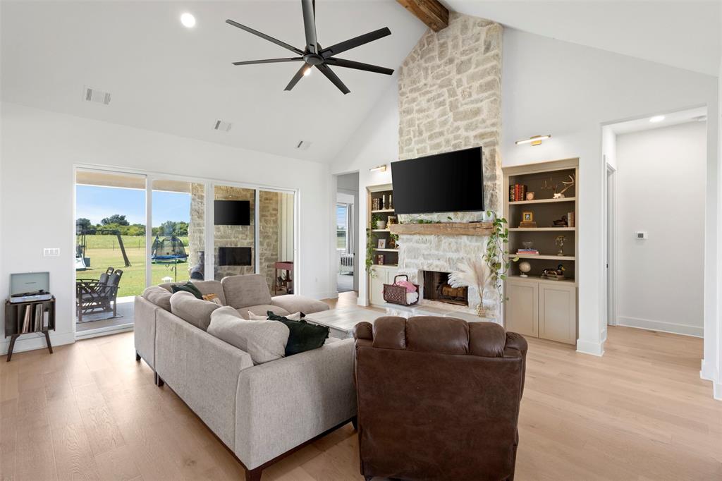 861 Brindley Road Maypearl, TX 76064 - Photo 5 of 36 Vaulted ceiling with exposed wood beam, stone fireplace with wood mantle, built-in shelving, wood-finish flooring, and sliding glass doors to outdoor patio