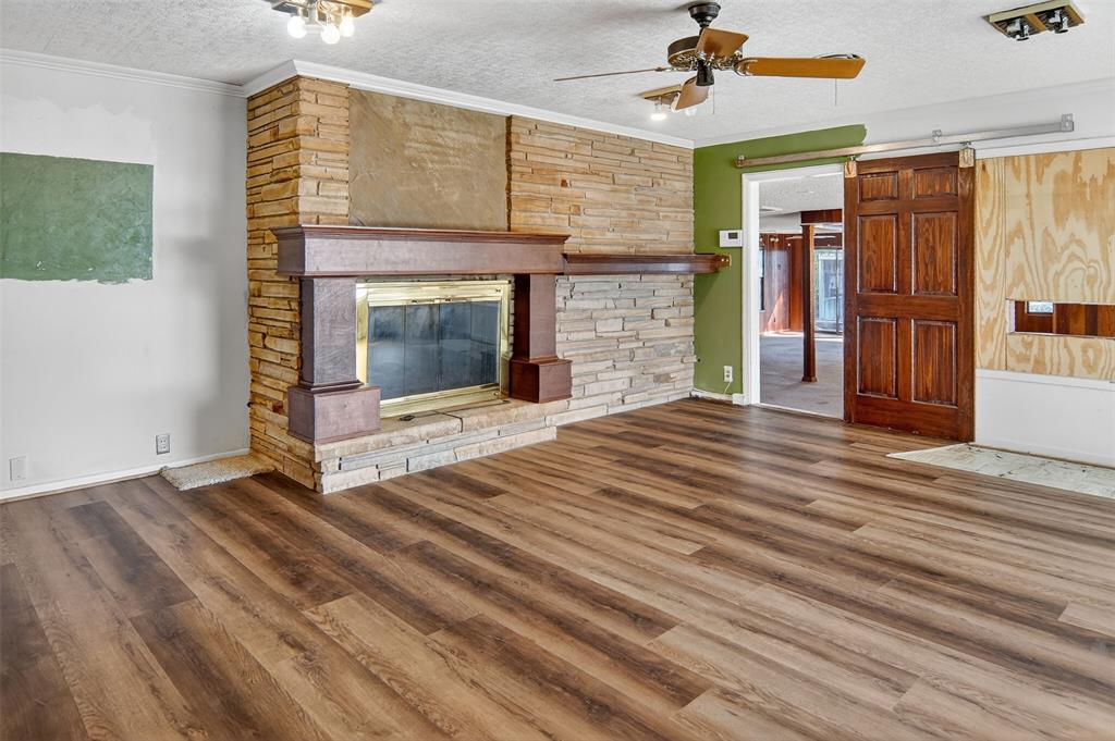 904 Northwest 7th Avenue Mineral Wells, TX 76067 - Photo 12 of 36 Unfurnished living room featuring a textured ceiling, a barn door, ornamental molding, a fireplace, and wood finished floors