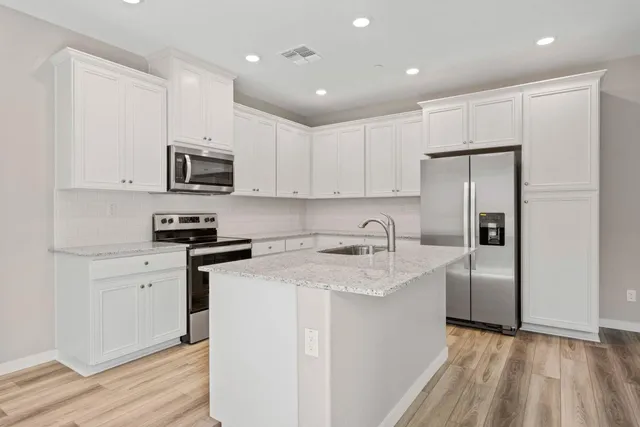 a kitchen with stainless steel appliances granite countertop a refrigerator a sink dishwasher a stove top oven a refrigerator and white cabinets with wooden floor