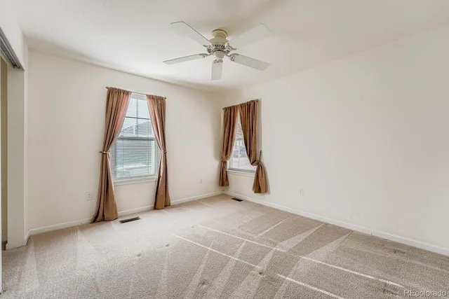an empty room with chandelier fan and windows
