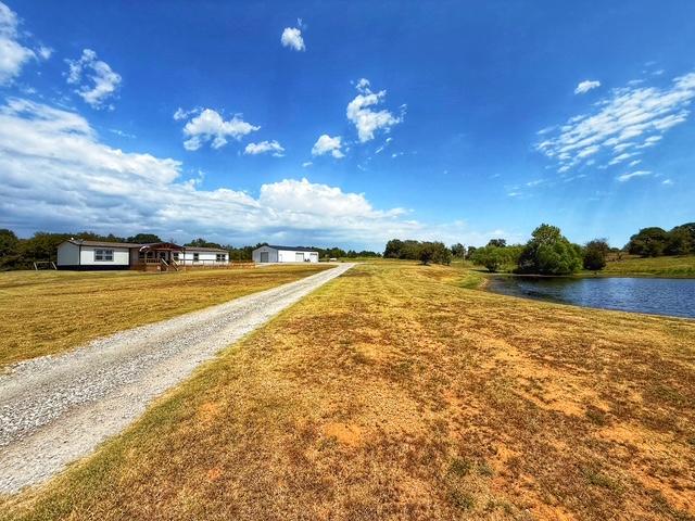 36469 1330th Road Wewoka, OK 74884 - Photo 10 of 39 Expansive property featuring a gravel driveway, a single-story residence with a covered porch, a separate outbuilding, mature trees, and a body of water